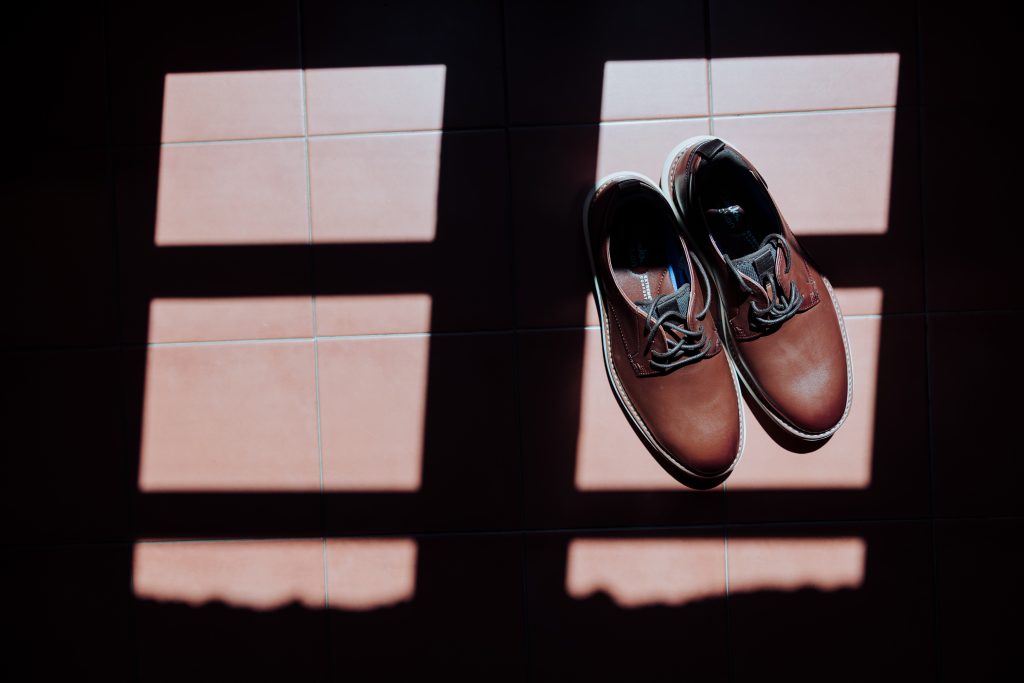 Zapatos de boda en luz natural sobre baldosas, con sombra y reflejo.
