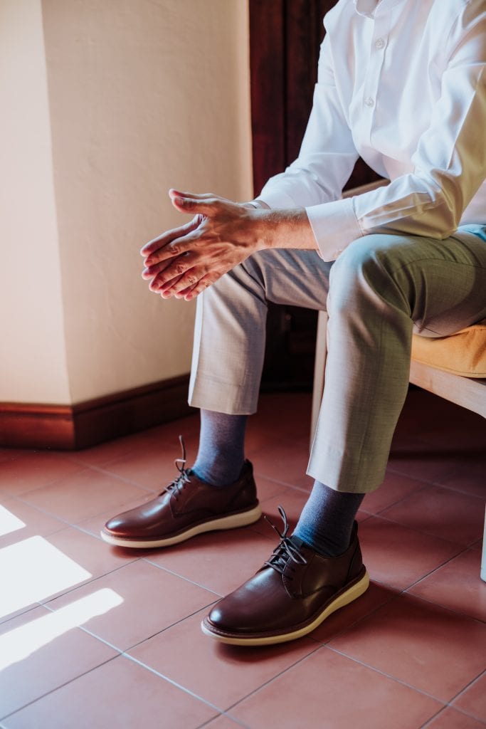 Hombre sentado preparándose para la boda, ajustando sus manos con elegancia.