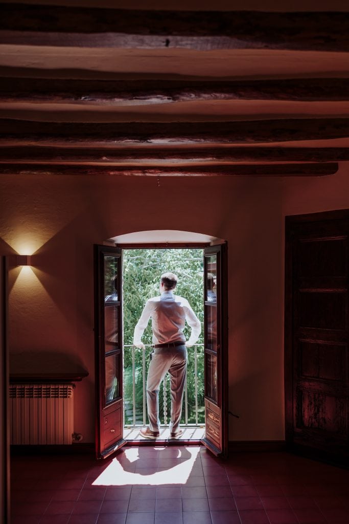 Mirada desde la ventana en una boda atípica, con un novio contemplando la naturaleza en un entorno í.