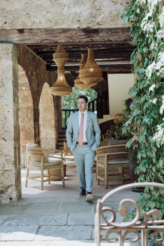 Novio con traje gris y corbata rosa en boda al aire libre.