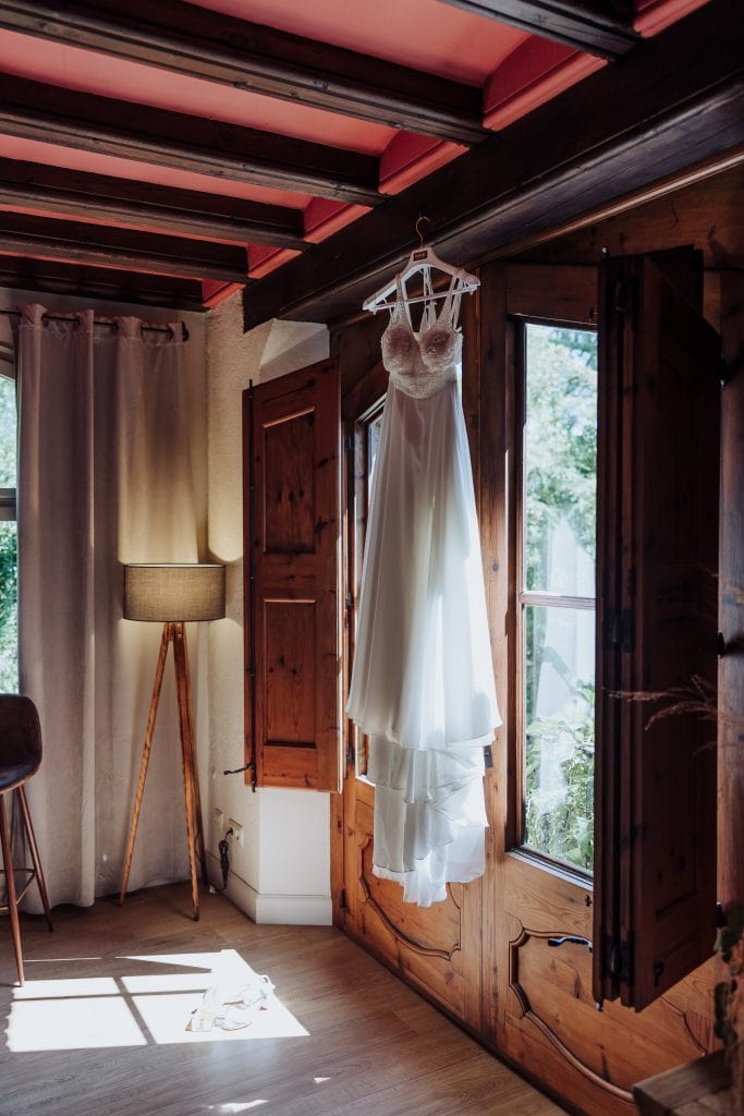 Vestido de novia elegante colgado en la ventana de una habitación rústica.