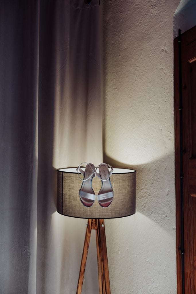 Zapatos de novia en lámpara de pie, decorando un rincón con cortinas y pared de textura suave.