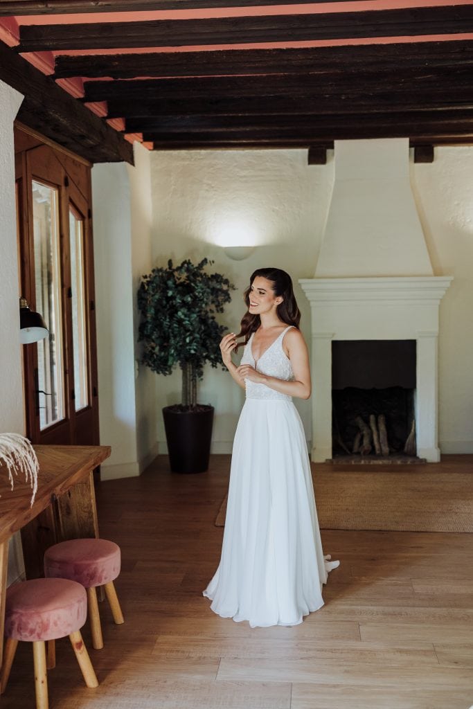 Vestido de novia blanco largo en interior con chimenea y decoración cálida.