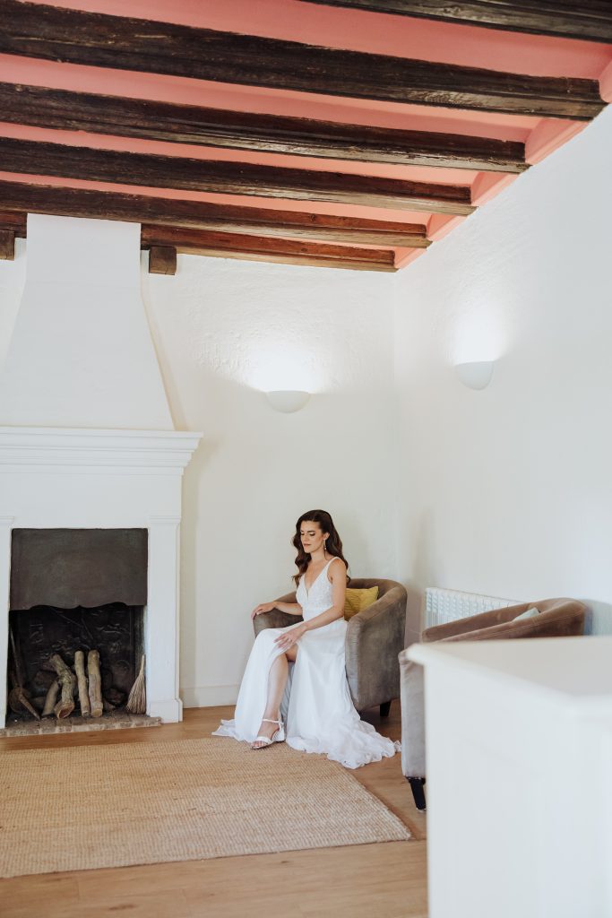 Boda en interior con chimenea y vigas de madera, novia en sofá, ambiente acogedor y elegante.