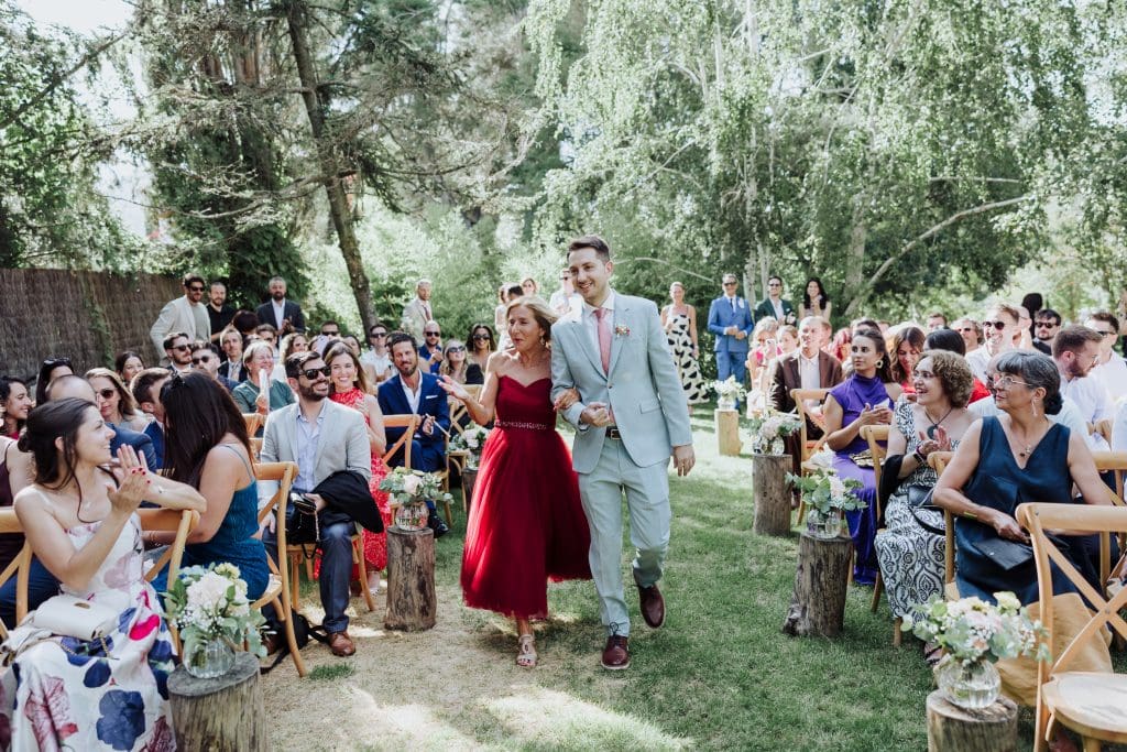 Boda al aire libre con pareja caminando entre invitados en un entorno natural.