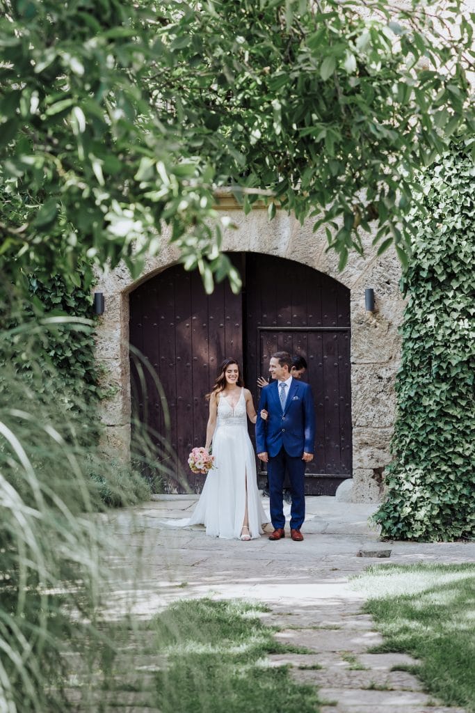 Pareja de recién casados en boda en jardín con puerta de madera antigua.