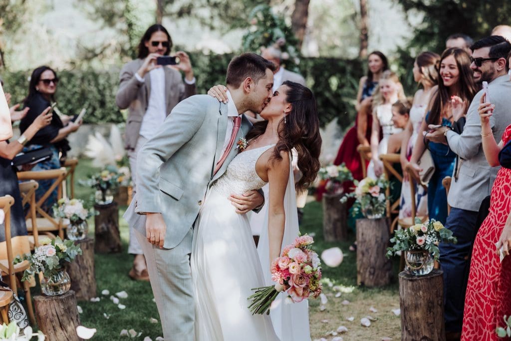 Boda en exterior con pareja en el centro, rodeada de amigos y decoración natural.