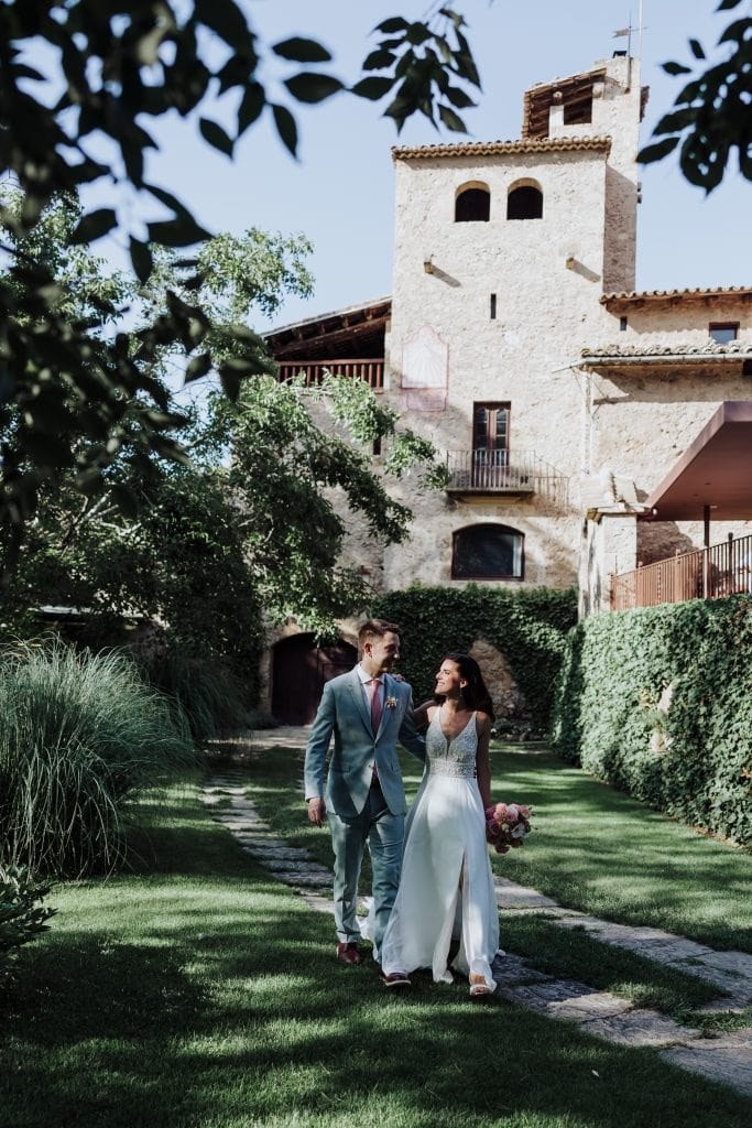 Boda en un entorno histórico con pareja caminando por jardines verdes y arquitectura antigua.