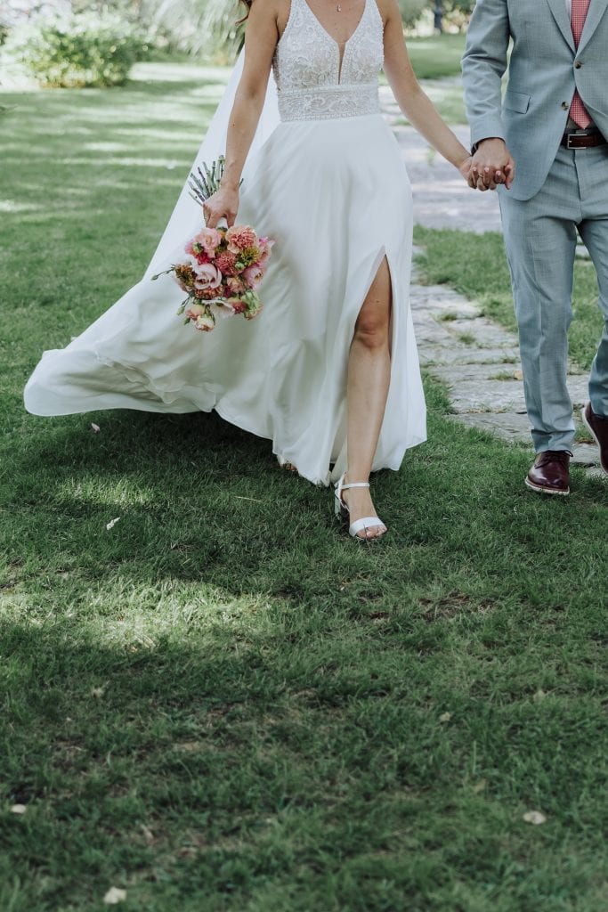 Boda en jardín con novia en vestido largo y novio en traje, caminando juntos.