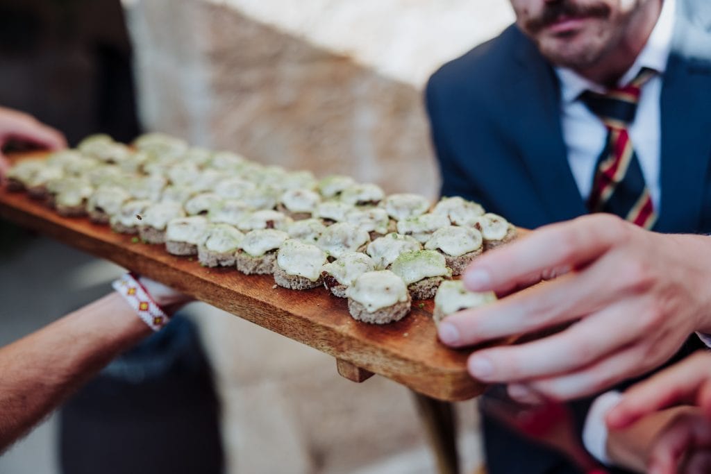 Bocaditos en una boda atípica, servidos en una bandeja de madera por un camarero.