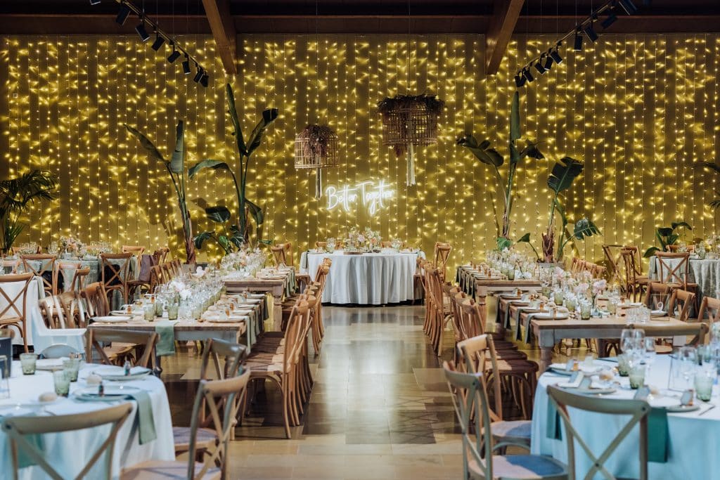 Decoración de boda con luces cálidas y mesas elegantes en interior acogedor.