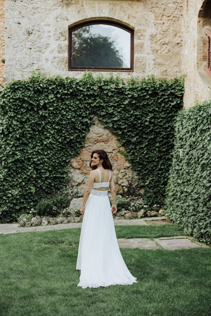 Boda en exterior con novia en vestido blanco en jardín con paredes de piedra y vegetación.
