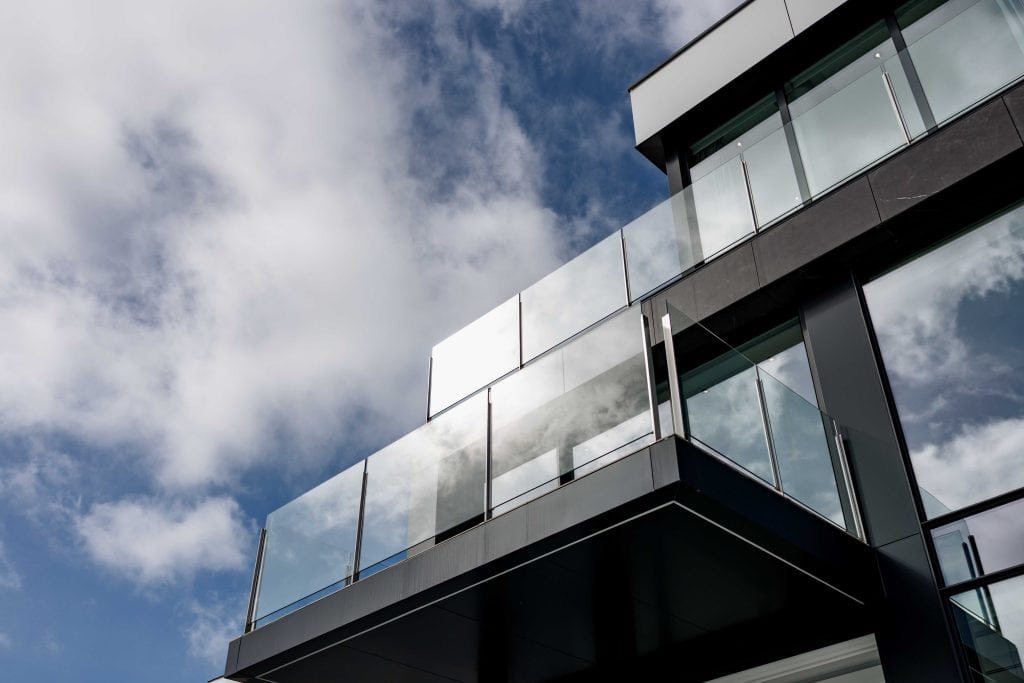 Edificio de apartamentos moderno con balcón de cristal y vistas urbanas en un día soleado.