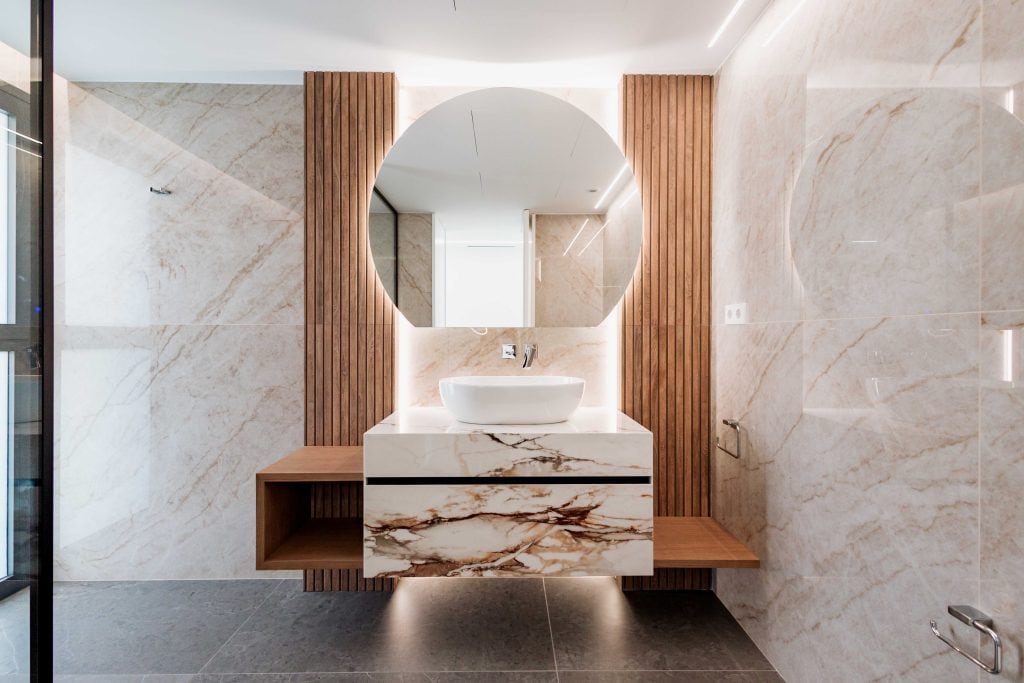 Lavabo moderno en baño elegante con espejo redondo y detalles de madera.