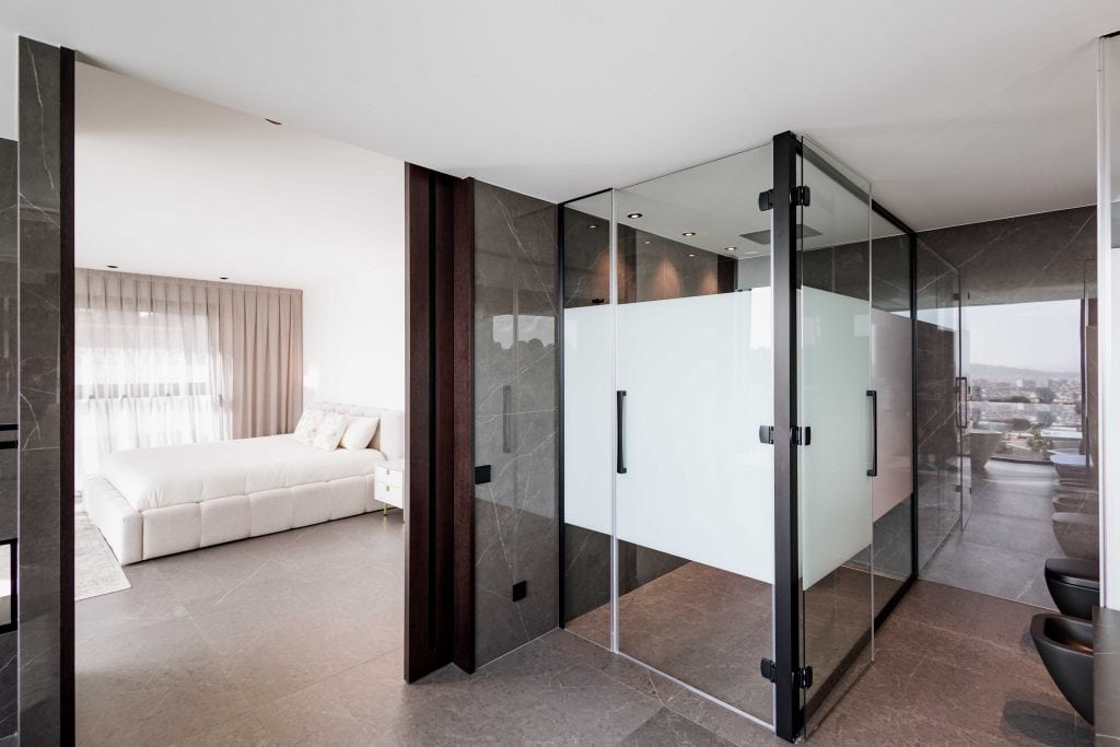 Suite nupcial moderna con ducha de cristal y vista a la ciudad.